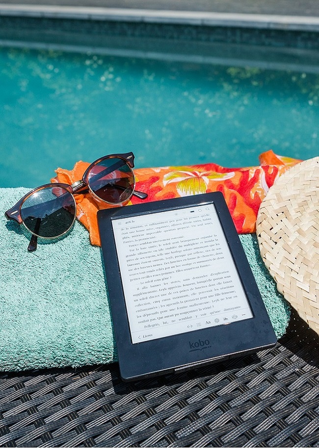 une liseuse, des lunettes de soleil et un chapeau de paille posés sur une serviette au bord d'une piscine
